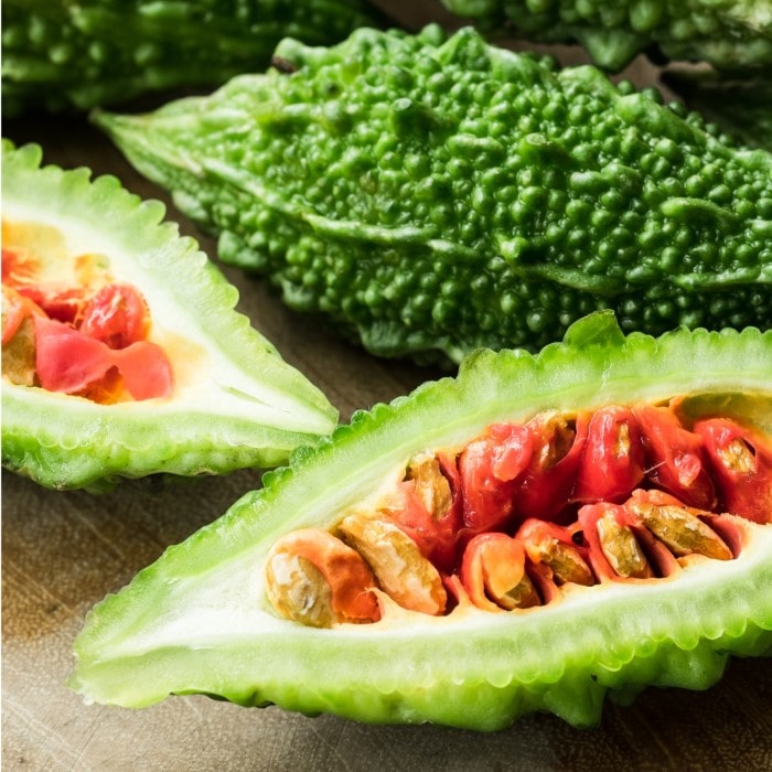 Almanac Planting Co: Sliced Ganjyu Bitter Melon showing bright green rind and red-orange seed interior on a cutting board