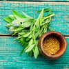 Almanac Planting Co: Fresh Fenugreek leaves and golden seeds displayed in a wooden bowl on turquoise surface