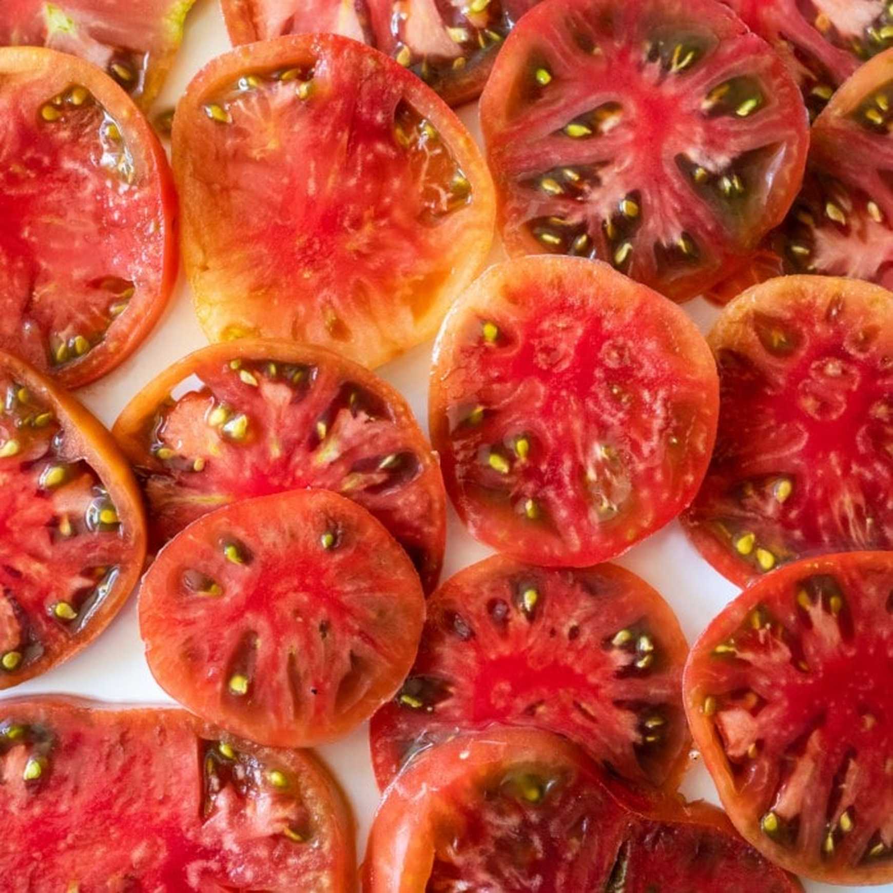 Almanac Planting Co Cherokee Purple Tomato. A bunch of tomato slices next to each other, with a slight amount of overlay. The background is white. 