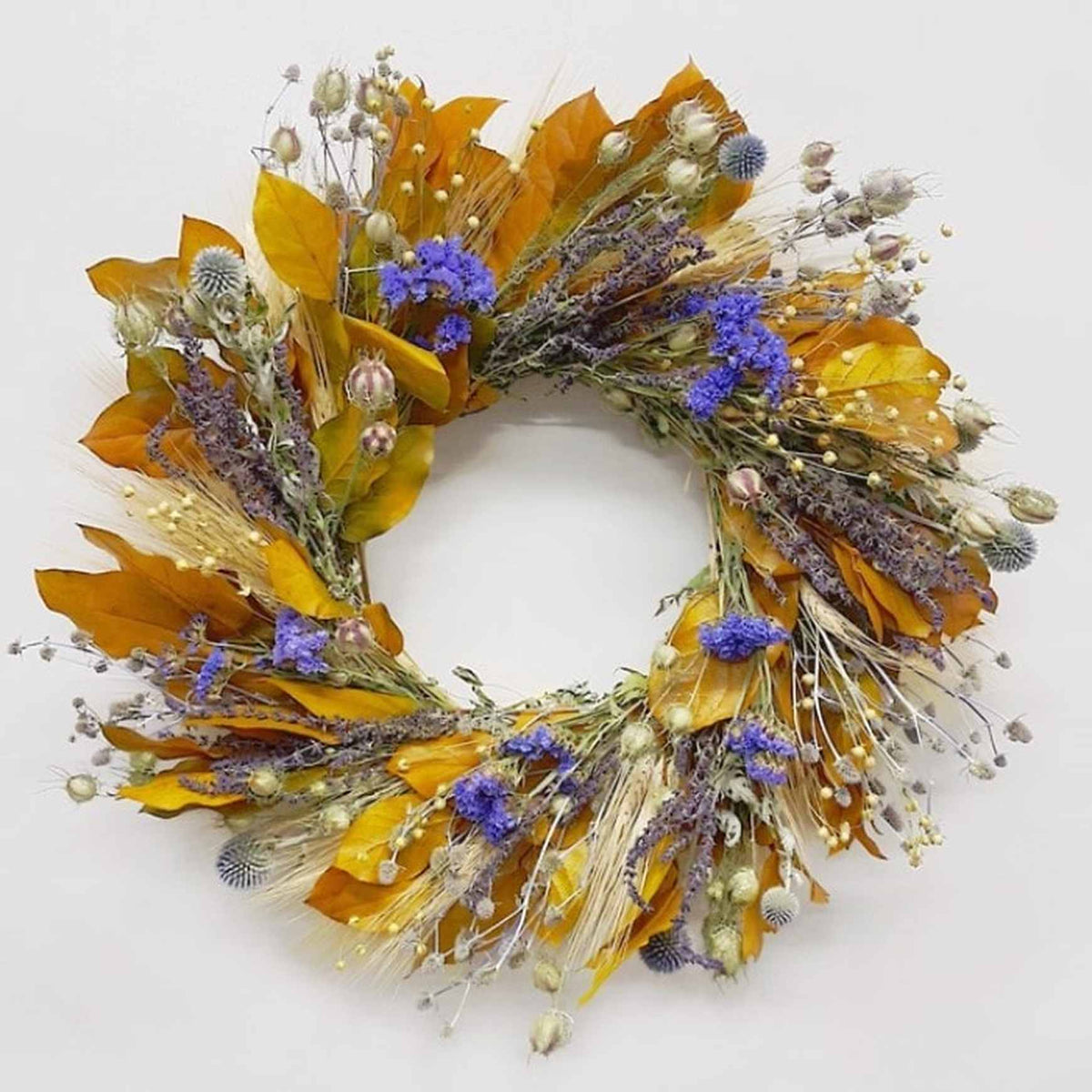 An indoor wreath made of blonde wheat, preserved yellow salal, eryngium, salvia, nigella, echinops, sinuata statice, and flax.
