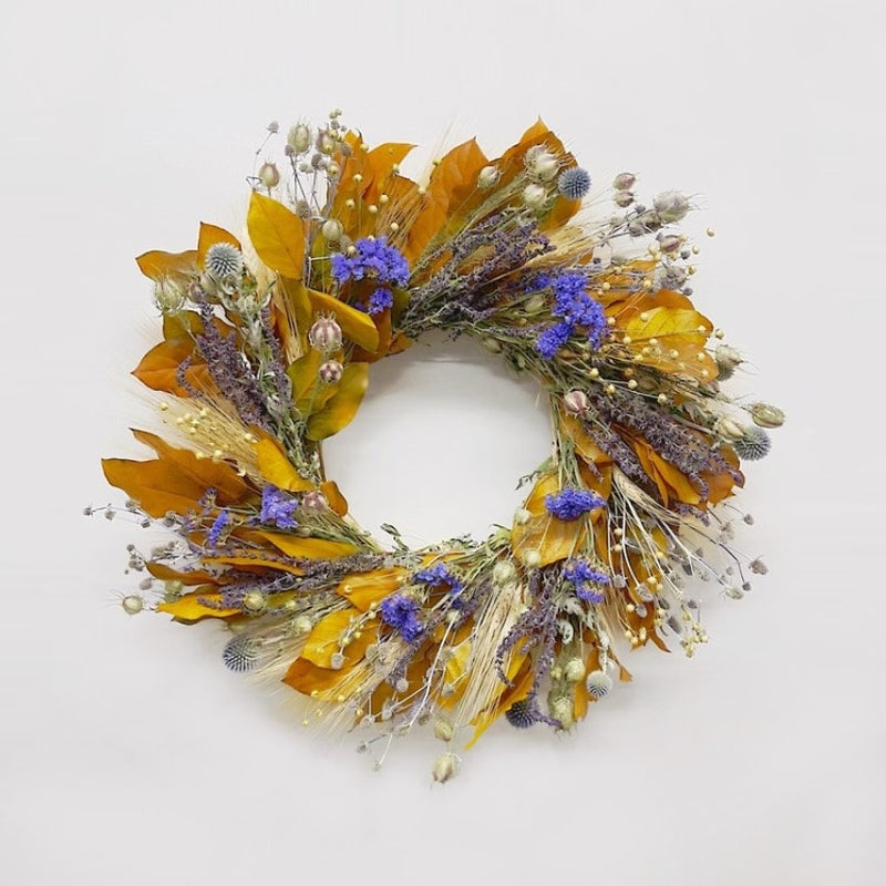 A hand made wreath constructed with blonde wheat, preserved yellow salal, eryngium, salvia, nigella, echinops, sinuata statice, and flax.