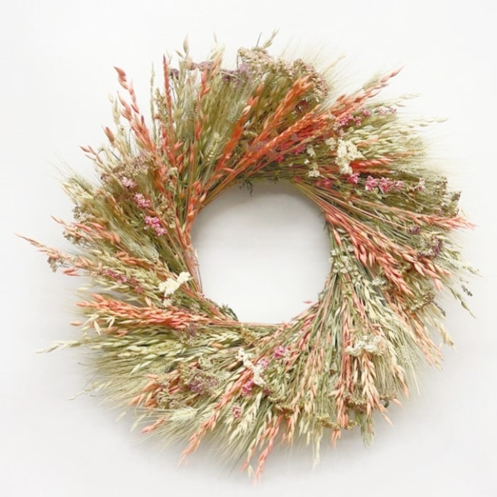 A fresh handmade wreath of avena oats, green wheat, orange colored avena oats, pink lankspur, natural color yarrow, and pearly everlasting.